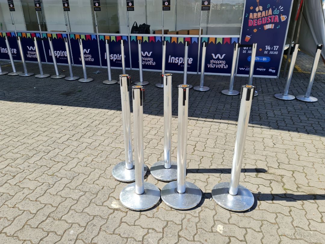 Pedestais cromados com fita retrátil preta organizando fila em evento